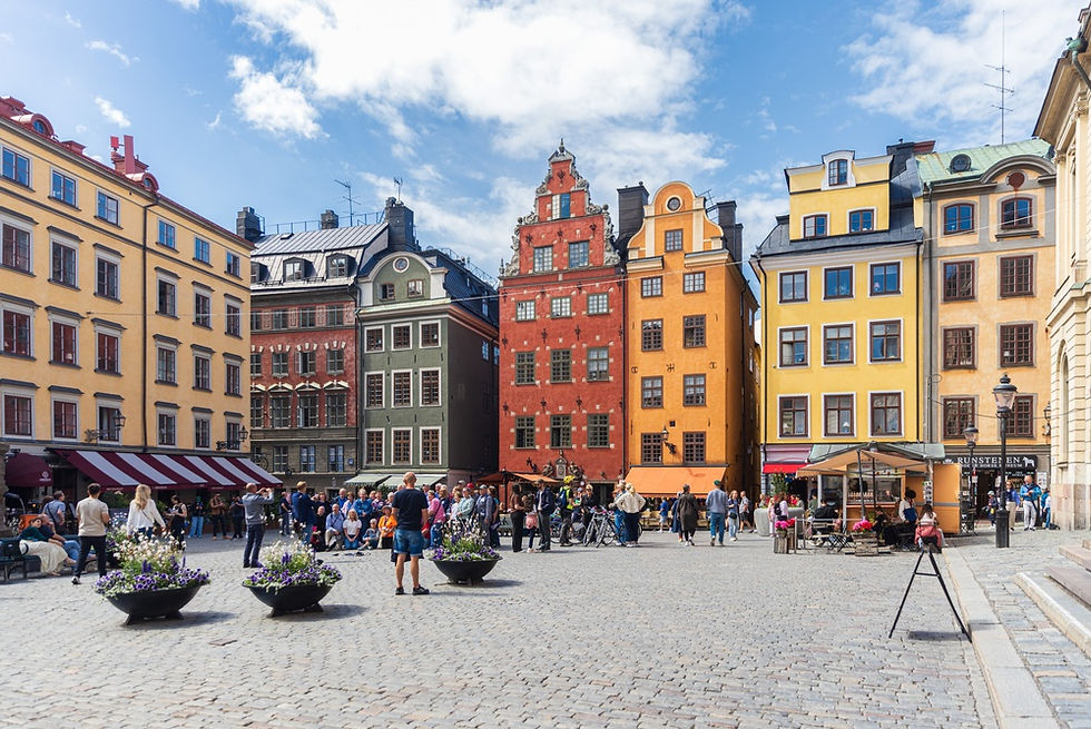 A bustling scene in Stockholm's historic Gamla Stan, with vibrant, colorful buildings framing the lively Stortorget square filled with people enjoying a sunny day.