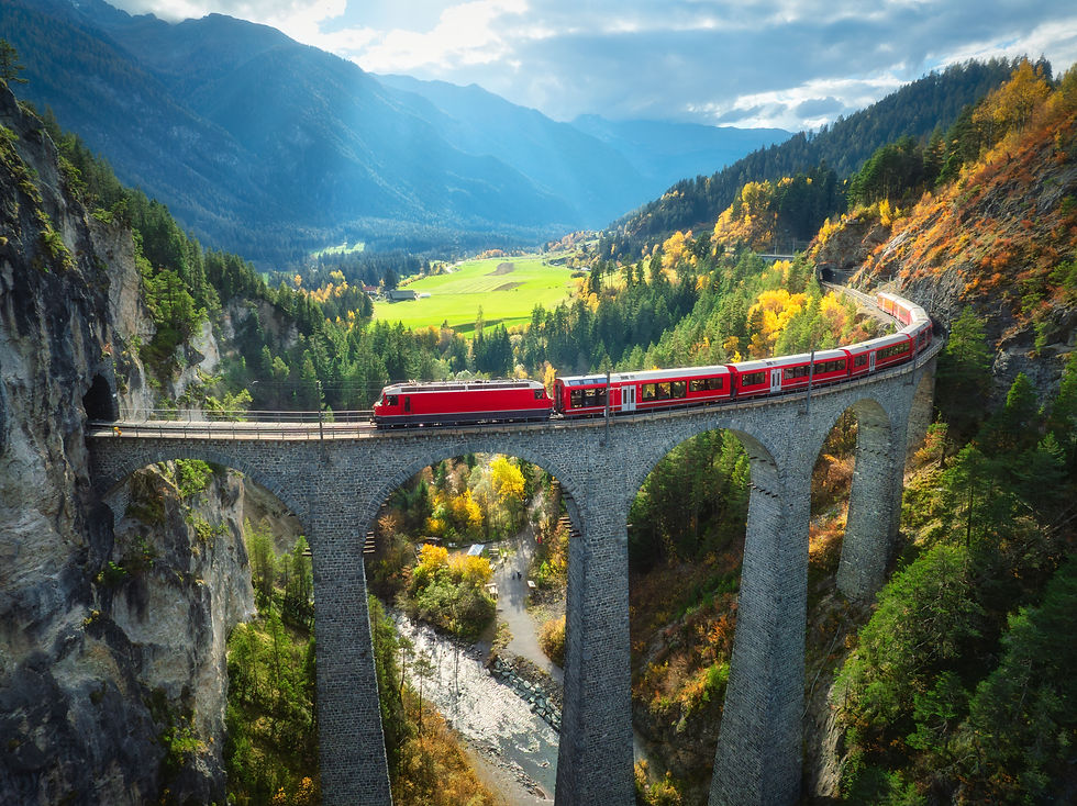 A vibrant red train crosses the dramatic Landwasser Viaduct, framed by the stunning autumn colors and breathtaking alpine scenery in Switzerland.