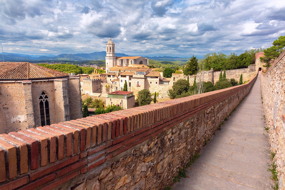 Historic charm abounds in Girona, Spain, as seen from the ancient city wall overlooking the iconic Cathedral and a canvas of rolling hills under dramatic skies.