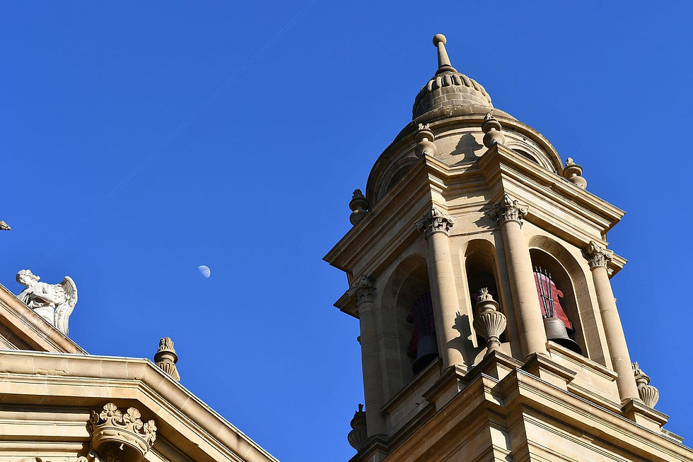 The elegant architecture of a historic bell tower is beautifully framed against a clear blue sky, with a half moon visible, adding a celestial touch to the scene.