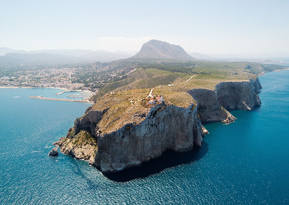 A breathtaking aerial view of the rocky coastline and vibrant blue waters near Cape located in Jávea, Spain. The striking cliffs and scenic landscape provide a stunning backdrop against the expansive Mediterranean Sea.