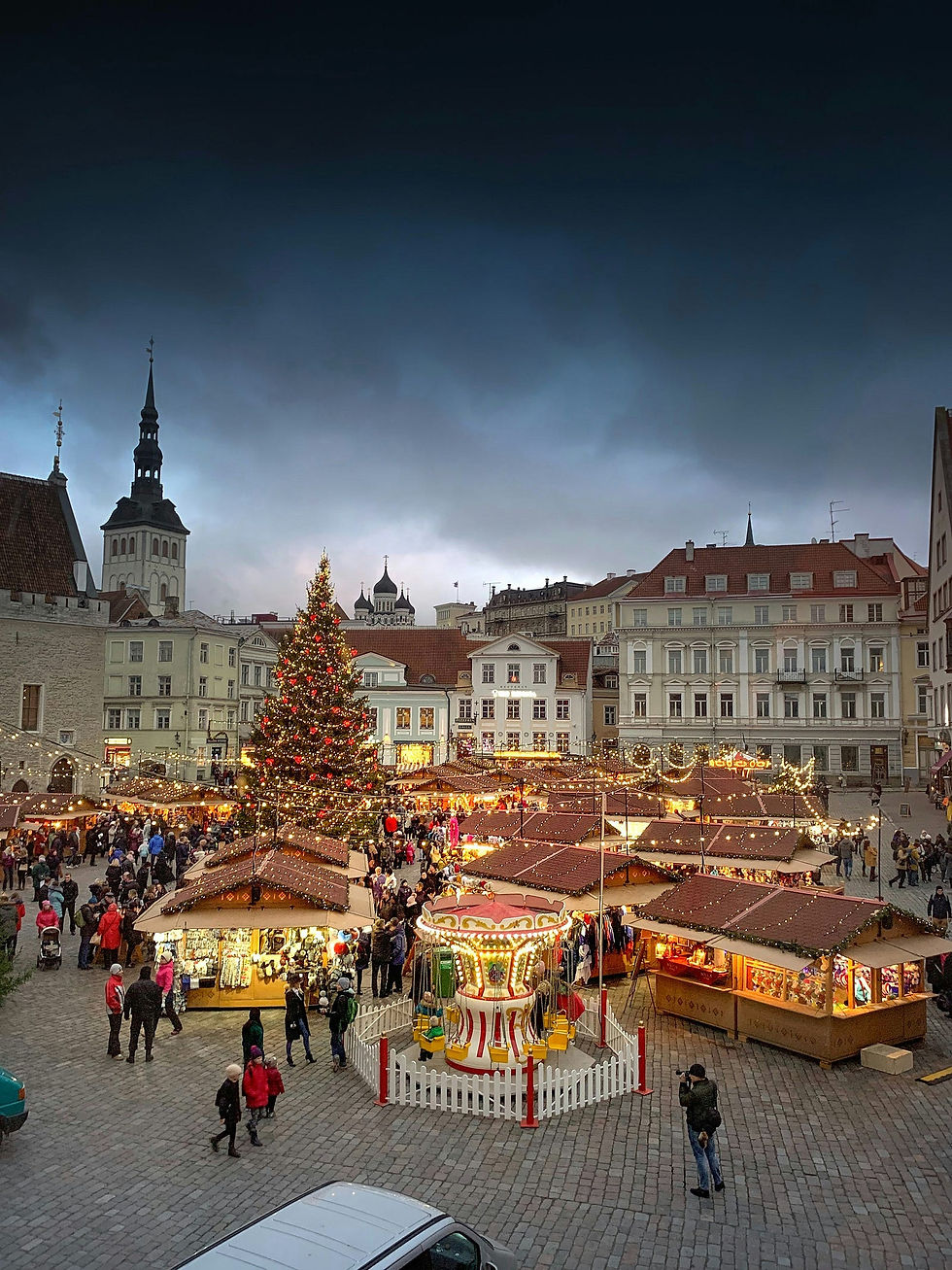 A bustling Christmas market in a picturesque European town square, adorned with a towering, illuminated tree and quaint wooden stalls. Visitors enjoy the festive atmosphere amidst twinkling lights, with a charming carousel adding to the magical winter scene.