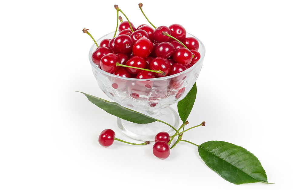 A glass bowl brimming with vibrant, ripe cherries sits elegantly alongside fresh green leaves on a pristine white background.
