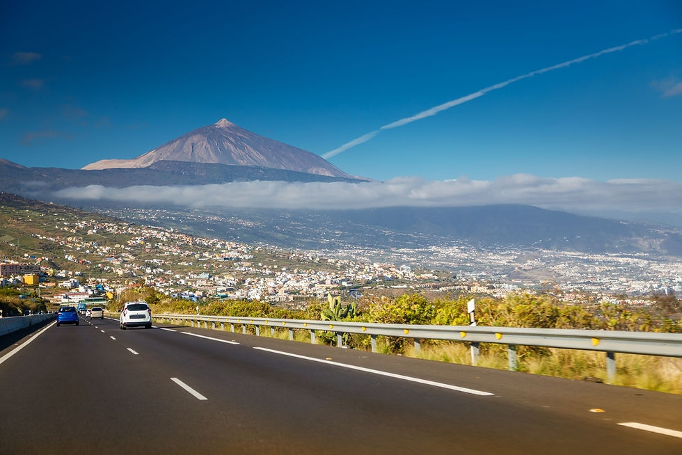 Cars travel along a scenic highway, with the majestic Mount Teide towering against a clear blue sky in the background on Tenerife, Canary Islands.
