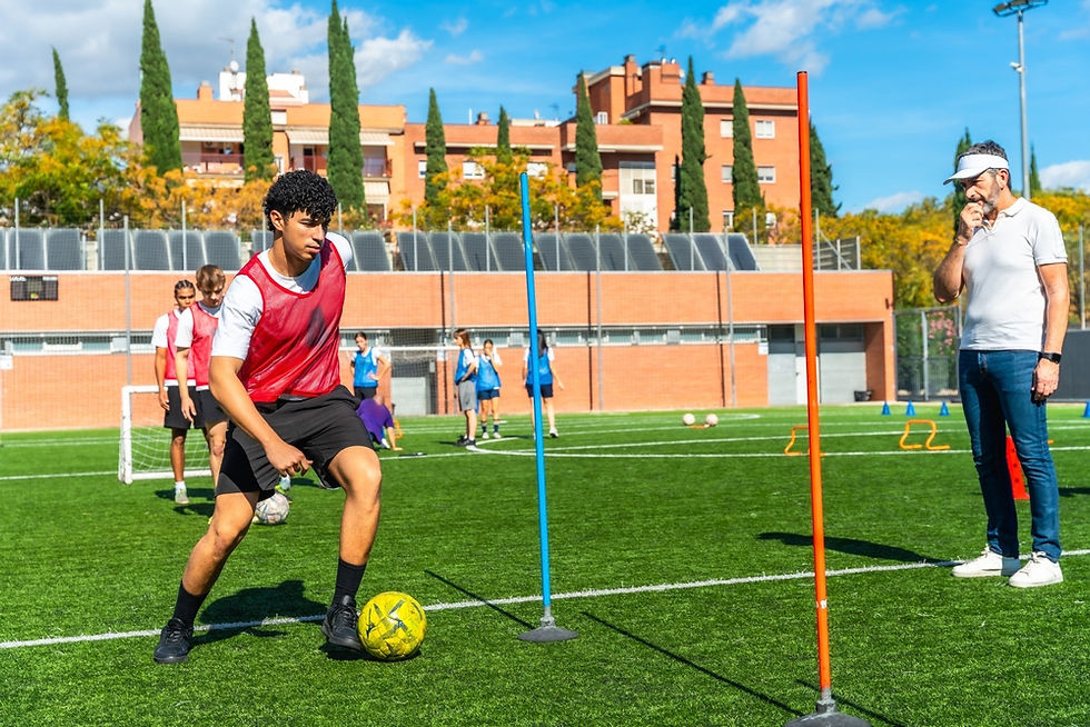 A young athlete navigates between agility poles on a sunny day, while a coach attentively observes from the sideline at a training session on a green sports field.