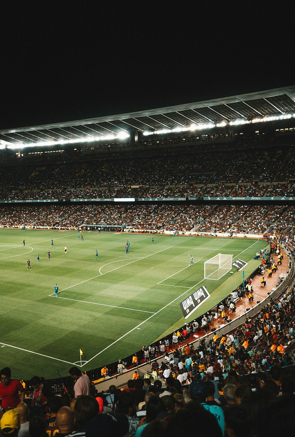 A packed stadium buzzes with anticipation as players take their positions on the vibrant green field during a night football match, under the bright floodlights.