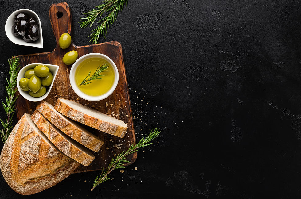 A rustic wooden board is artfully arranged with freshly sliced bread, a bowl of olive oil garnished with rosemary, and small dishes of green and black olives, creating a perfect Mediterranean appetizer setting.