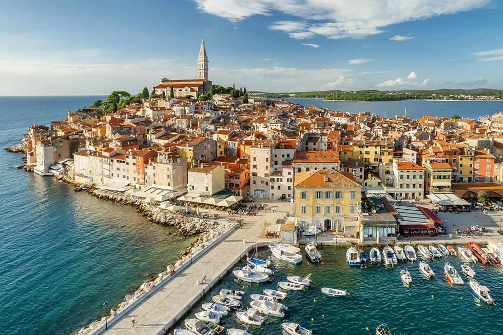 A stunning aerial view of Rovinj, Croatia, showcasing the charming old town with its iconic bell tower and colorful buildings surrounded by the Adriatic Sea, under a clear blue sky.