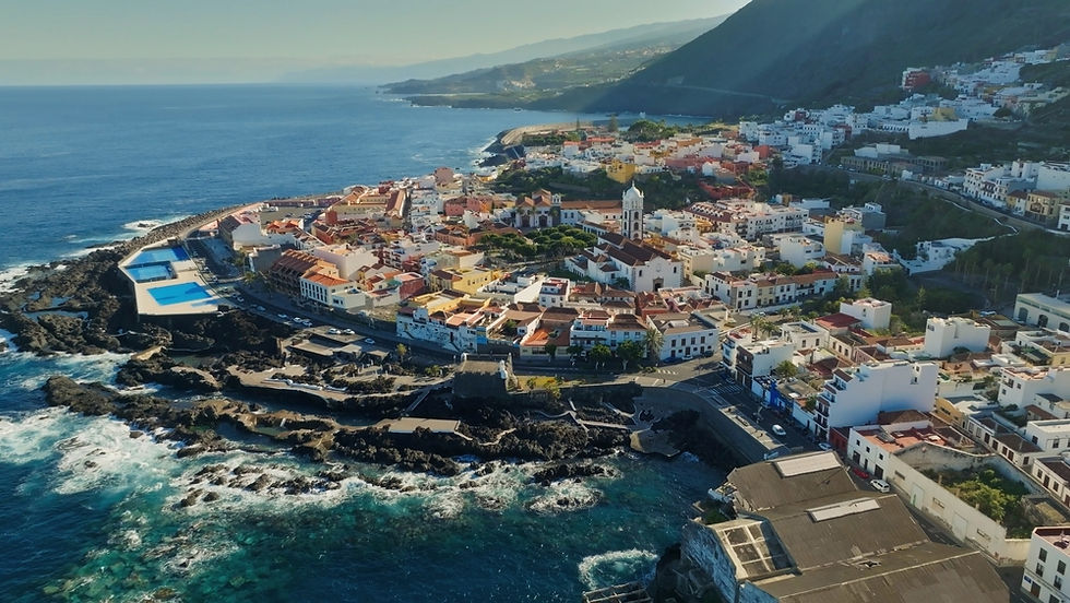 Aerial view of Garachico, a picturesque coastal town in Tenerife, showing its charming architecture and rugged shoreline under a clear blue sky.