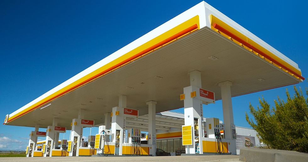A modern gas station with multiple fuel pumps stands under a clear blue sky, featuring a distinctive yellow and red color scheme.