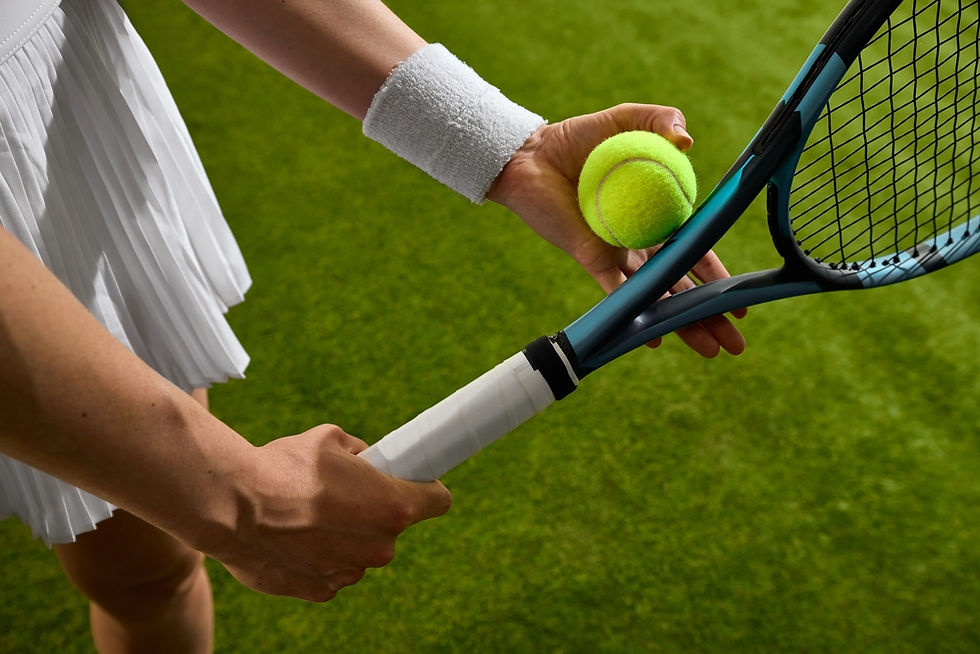 A tennis player wearing a white outfit prepares to serve, holding a racket and a bright yellow tennis ball on a lush green court.