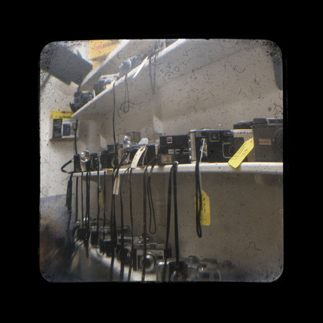 A shelf with many small cameras with yellow tags.