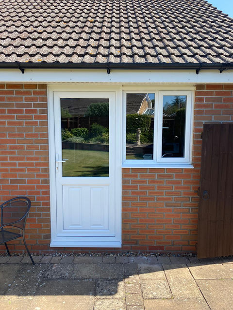 White PVC-U back door with large glazed panel beside matching casement window on brick bungalow.