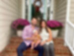 husband and wife with baby on front porch with dog in window