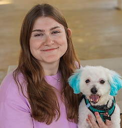 Girl with brown hair holding a small white dog with blue ears