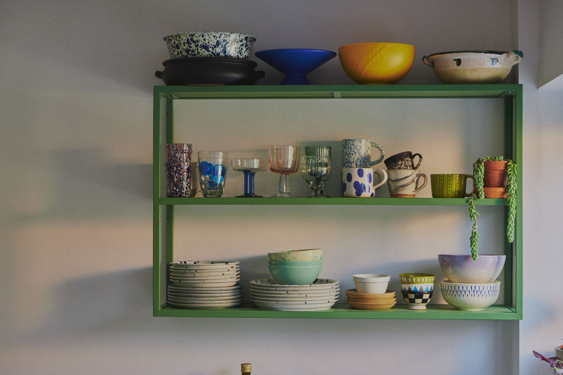 This custom sage green galley kitchen combines earthy tones with thoughtful design for a warm, character-filled space. By removing a wall to join the kitchen and dining areas, the layout was dramatically improved with minimal structural work. The steel frames were powder-coated in RAL 6011, with birch plywood fronts stained to match — allowing the natural grain to show through and soften the industrial feel. A raw white quartz worktop adds warmth and texture, while open shelving displays the client’s handmade crockery and glassware. The end unit cleverly hides the washing machine and serves as a kitchen island, subtly dividing the space. Quarry tiles and vintage furniture add charm, and a signature freestanding larder provides generous food storage for family life. A practical, beautiful kitchen with natural materials, bespoke craftsmanship, and timeless colour.