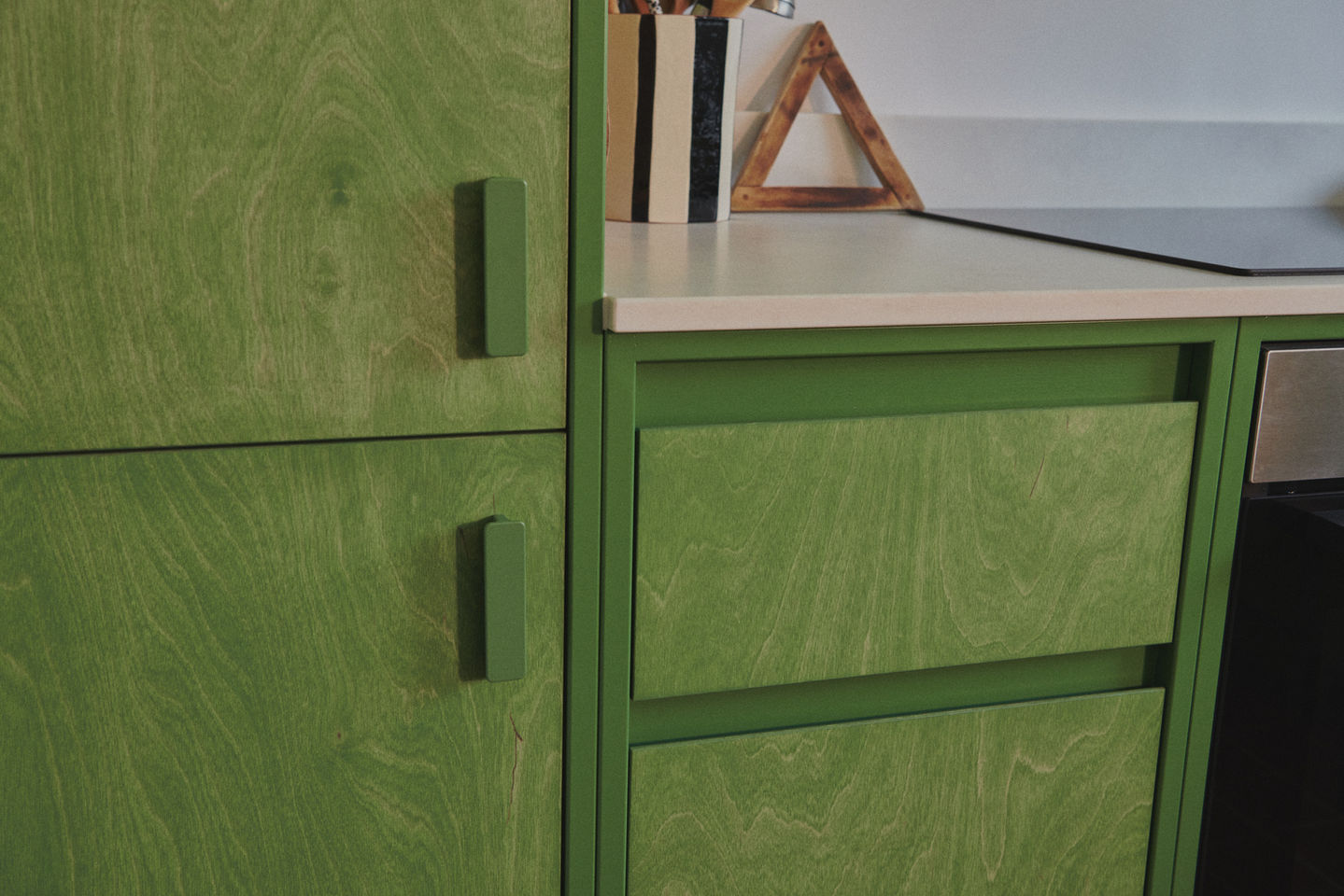 Sage green galley kitchen with RAL 6011 steel frames, stained birch plywood fronts, raw white quartz worktop, open shelving, and quarry tile floor.