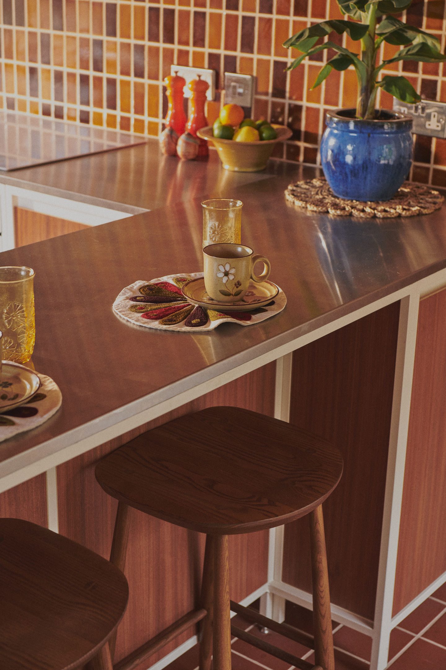 Mid-century kitchen with RAL 9010 steel frames, Sapele veneer, reeded glass wall units, stainless steel worktop, teak ceiling panels, and vintage-style tiles.