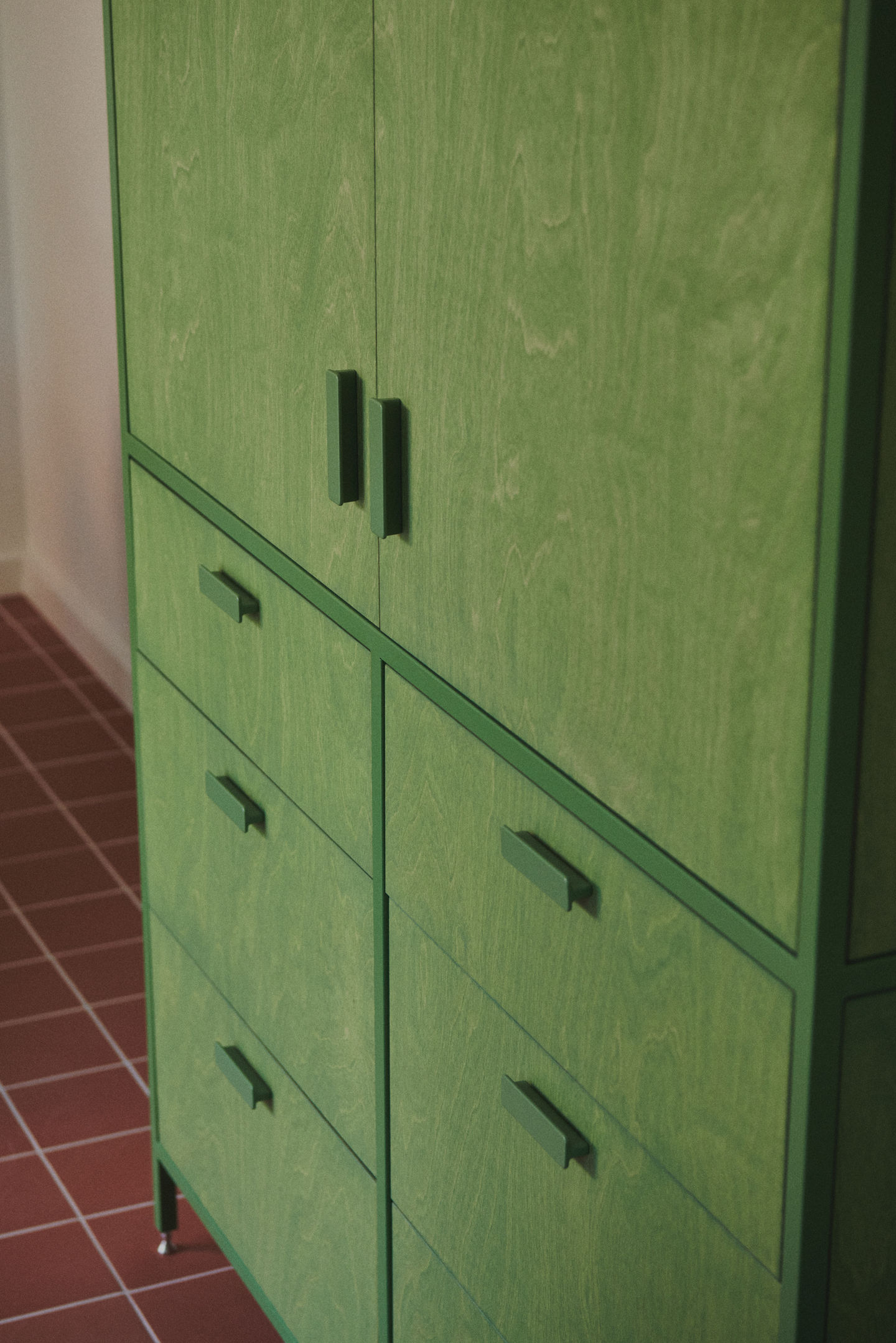 Sage green galley kitchen with RAL 6011 steel frames, stained birch plywood fronts, raw white quartz worktop, open shelving, and quarry tile floor.