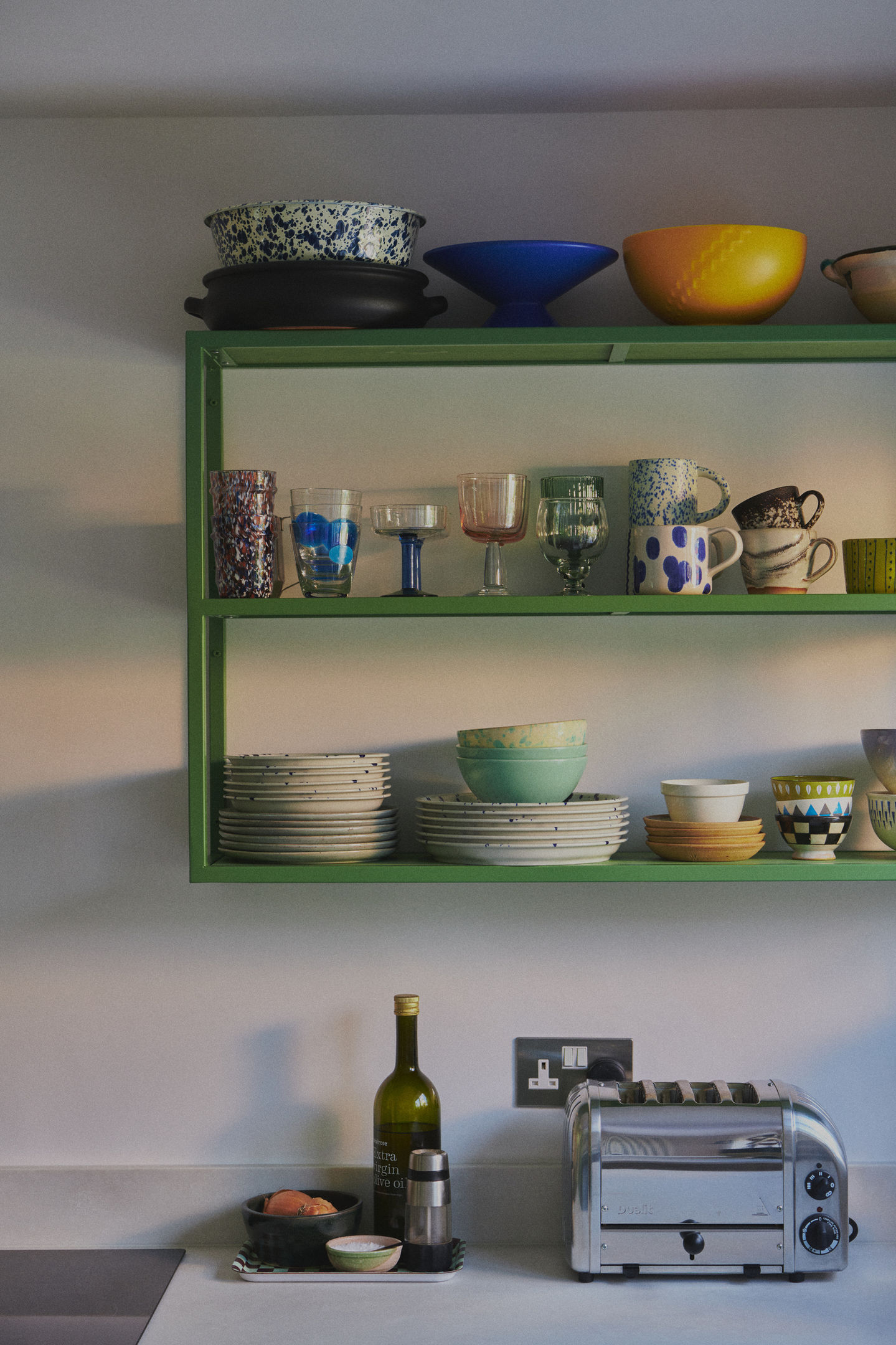 Sage green galley kitchen with RAL 6011 steel frames, stained birch plywood fronts, raw white quartz worktop, open shelving, and quarry tile floor.
