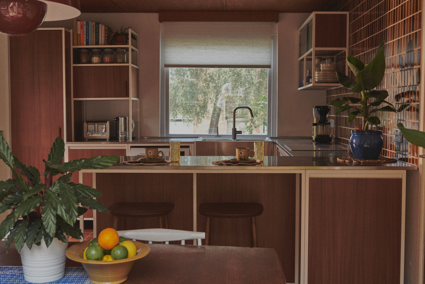 Mid-century kitchen with RAL 9010 steel frames, Sapele veneer, reeded glass wall units, stainless steel worktop, teak ceiling panels, and vintage-style tiles.