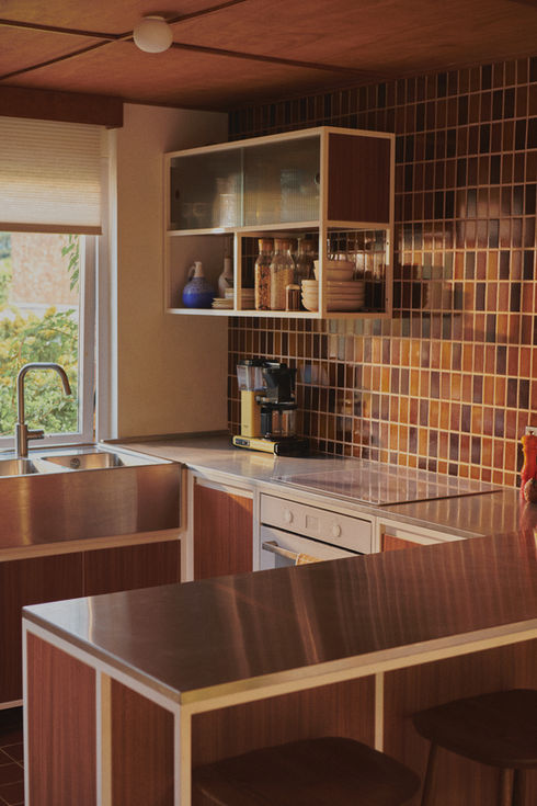 Mid-century kitchen with RAL 9010 steel frames, Sapele veneer, reeded glass wall units, stainless steel worktop, teak ceiling panels, and vintage-style tiles.