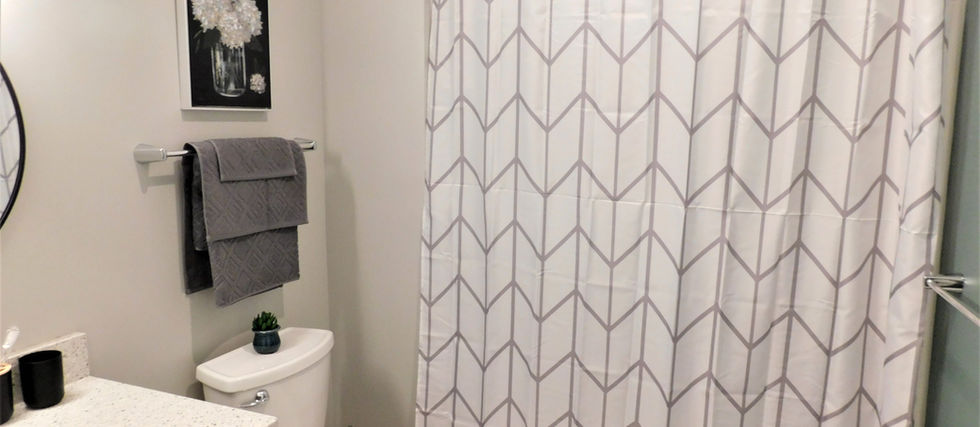 A bathroom with a single sink with cabinets under it, a toilet, next to a shower and tub combo with a white and grey striped shower curtain