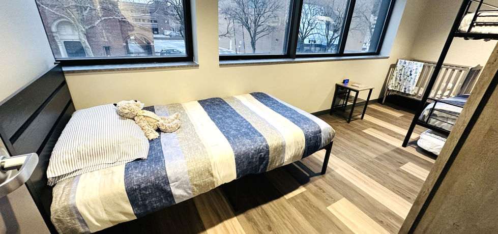 A bedroom with a double bed, a set of bunk beds, and a crib with grey and blue bedding for all beds and a teddy bear on the pillows.