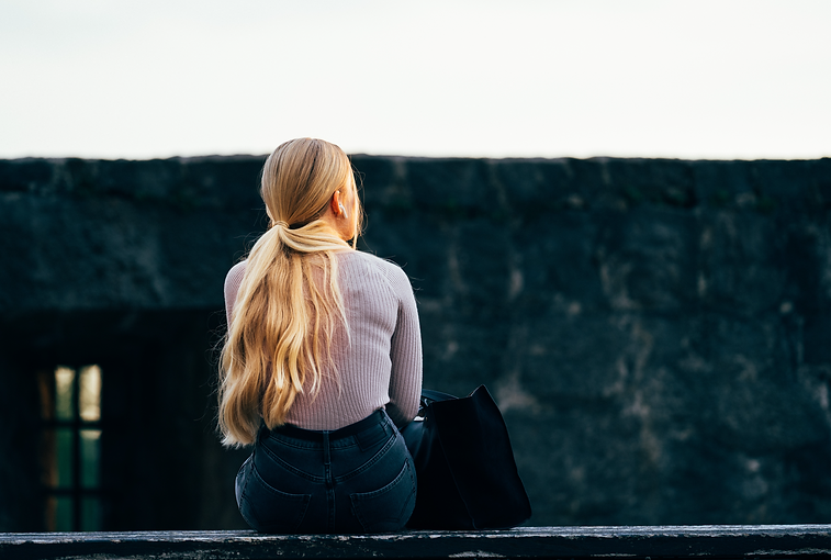 woman in white long sleeve shirt and black denim jeans sitting on gray concrete wall durin