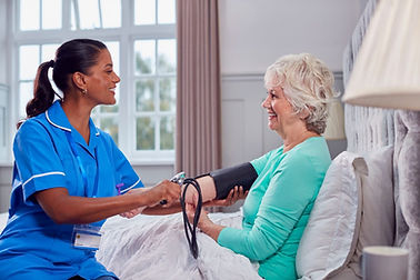 senior-woman-at-home-in-bed-having-blood-pressure-taken-by-female-care-worker-in-uniform.j