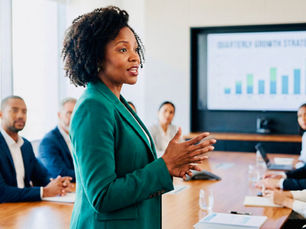 A woman in a green blazer presents in a boardroom with colleagues around a table. A screen shows a "Quarterly Growth Strategy" chart.