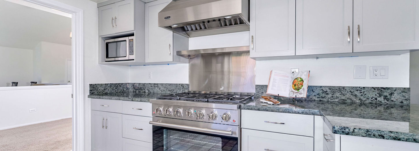 Kitchen cooking area with stainless steel range, vent hood, light gray cabinetry, and granite countertops.