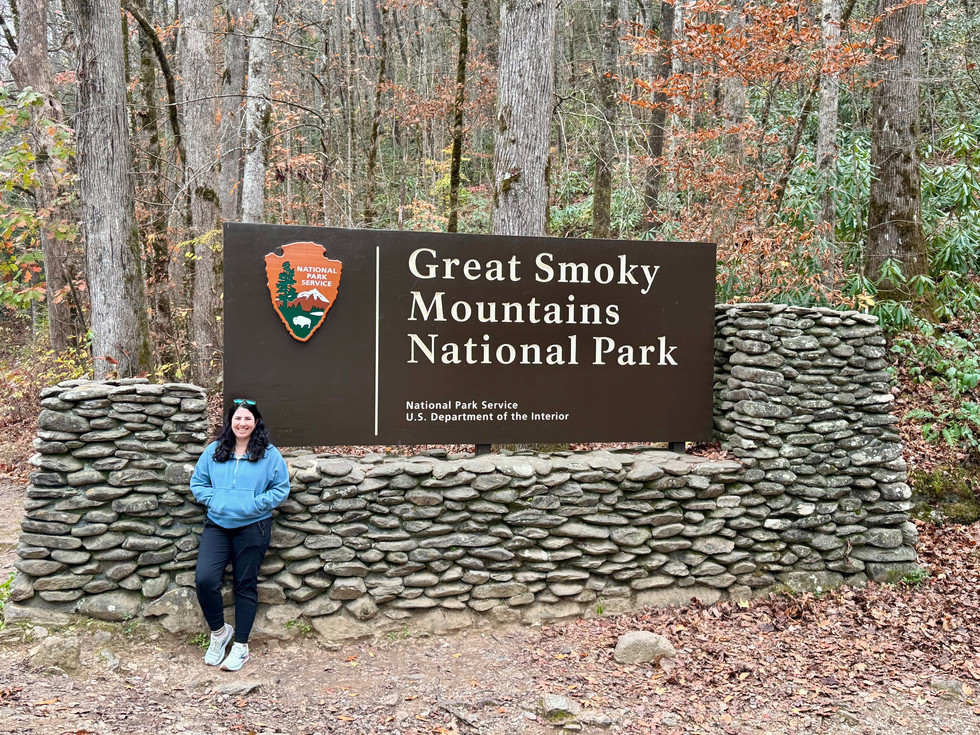 A woman standing in front of the Great Smoky Mountains national park entrance sign