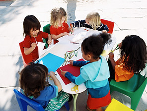 6 young girls sitting around a table painting and drawing art.