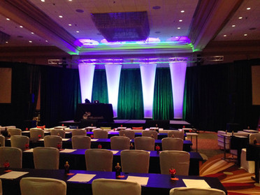 Innovative spandex stretch forms with ambient uplighting by Be Bright Events create a serene backdrop for a client's corporate event stage