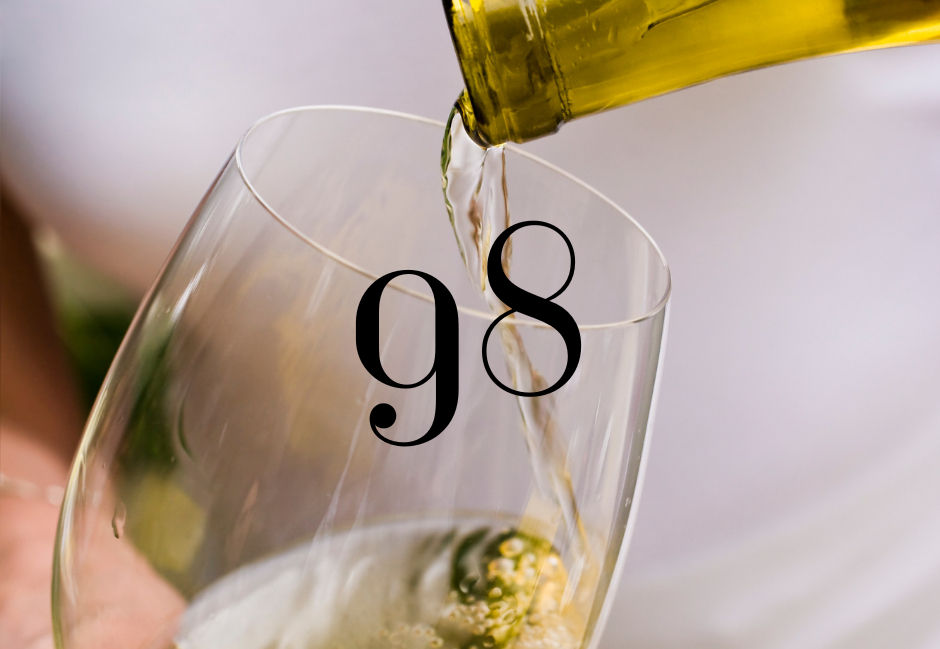Una copa de vino blanco siendo servida de una botella, con el número 98 superpuesto sobre la imagen.