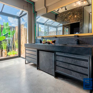 Banheiro estilo loft de Nova York: concreto aparente no piso e paredes, móveis em tons de grafite, grandes panos de vidro integrando o jardim externo e cobertura em vidro — sofisticação e contemporaneidade