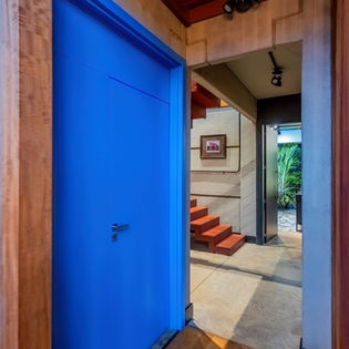 Detalhe da porta azul do lavabo criando contraste com o piso em cimento queimado e paredes em paineis de concreto aparente. Uma casa de campo conceitual com assinatura Isabella Dalfovo Arquitetura