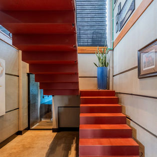 Escada em concreto pintada de vermelho, destaque do hall de entrada, trazendo contemporaneidade e sofisticação ao contrastar com as paredes e o piso em concreto aparente.