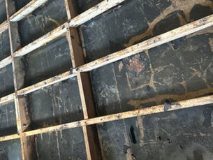 Wooden beams in a grid pattern, overlaying a dark, worn surface. The setting is a construction site for renovation project, made by design build contractors Built with Love.