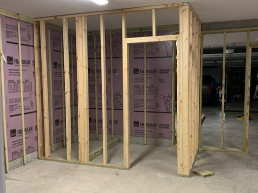 Wooden framework for a room under construction in a garage with pink insulation and tools on the floor under bright overhead light. The image represents bathroom renovations for elderly made by Built with Love.