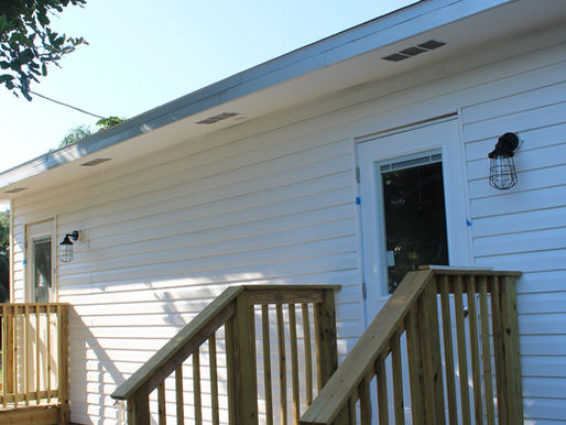 White house with wooden steps and railings, surrounded by greenery. Clear blue sky and sunlight create a calm, inviting atmosphere. The ADU picture was taken by Built With Love in St. Petersburg, Florida. The image is used to represent accessory dwelling unit builders near me.
