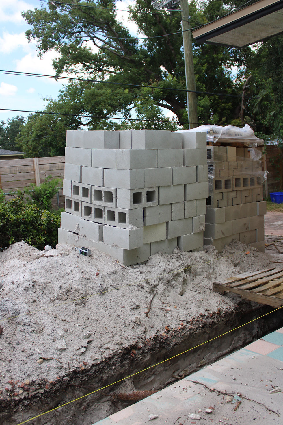 Stacked concrete blocks on sand, surrounded by construction debris and a wooden pallet. Trees and fence in the background; calm setting. The picture was taken by Built with Love for HB Design and Engineering in St. Petersburg, Florida, and its used to represent civil engineer vs structural engineer.