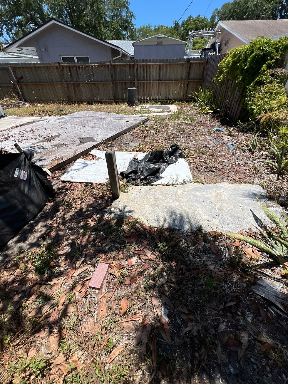 Overgrown backyard with scattered debris, a damaged wooden fence, and two houses in the background, under a clear blue sky. The image represents a exterior remodeling contractor. The picture was taken by "Built with Love".