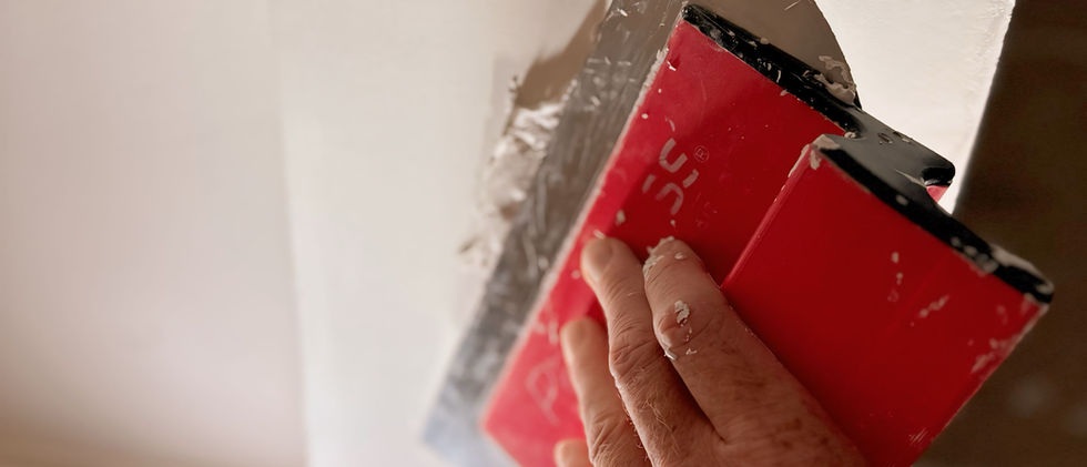 Un artesano reparando el yeso de una pared con una espátula roja, alisando las imperfecciones para garantizar una superficie perfecta.