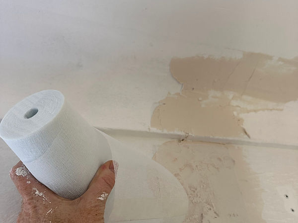 Bande de renfort pour fissure présentée devant un support intérieur fissuré et dégradé avant reprise à l’enduit.