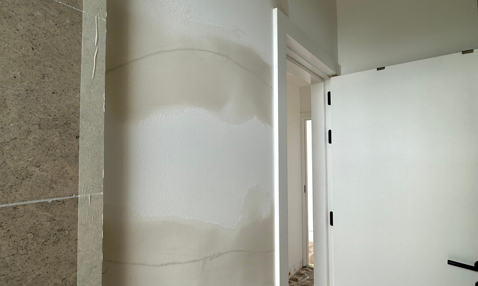 Immagine di una crepa sul muro del bagno. La fessura è visibile su una superficie bianca e sembra seguire una linea verticale irregolare. La parete presenta segni di deterioramento dovuti all'umidità. Sullo sfondo una porta bianca è aperta e rivela un'altra stanza. La crepa è pronta per essere riparata da un artigiano professionista, utilizzando tecniche specialistiche per garantire una finitura liscia e durevole. Questa scena illustra il tipo di problema comunemente affrontato da ASF Peinture et Décor nei loro progetti di ristrutturazione e riparazione di interni.