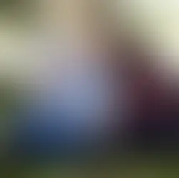 Image d'un couple présentant des traits de la trisomie 21, assis affectueusement dans l'herbe au pied d'un grand arbre dans un parc. L'homme, souriant, tient un cornet de glace, sa tête posée contre celle de sa compagne qui rit doucement en tenant une petite brindille. Ils portent des vêtements décontractés.