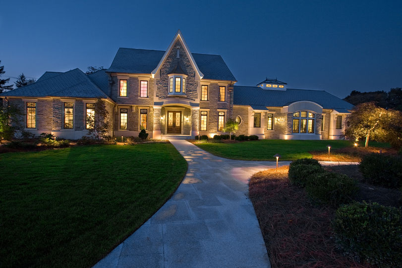 A large home made of stone in the evening with warm driveway lights and porch lighting