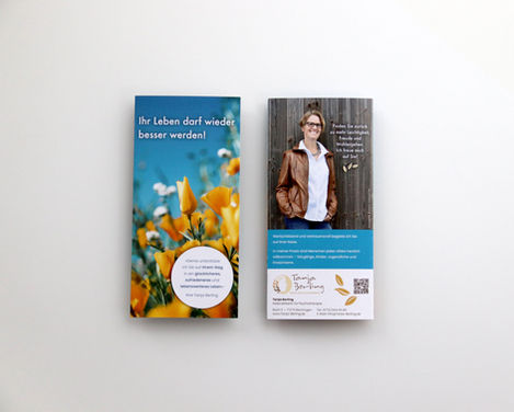 Das geschlossene Faltblatt im Endformat DIN lang hoch liegt mit Titelseite und Rückseite nebeneinander auf einem neutralen Hintergrund.